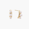 14K gold-plated curved stud earrings with three white freshwater pearls aligned vertically on cream background