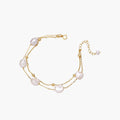 Double-strand gold bracelet with irregular baroque pearls and smooth freshwater pearls on cream background.