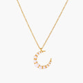 Gold crescent moon pendant with graduated white pearls on delicate chain against cream background